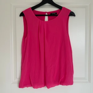 Rosa ärmlös blus - Säljer en snygg rosa ärmlös blus med rund halsringning och lätt rynk framtill. Blusen har en liten öppning med knapp i nacken och är tillverkad i ett tunt, luftigt material. Perfekt för varma dagar eller att styla lager på lager.