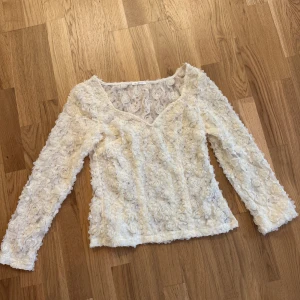 Ida Sjöstedt blus - Säljer en vit blus med v-ringning och långa ärmar. Blusen är täckt av vackra spetsdetaljer i blommönster. Perfekt för dig som vill ha en feminin och elegant topp.