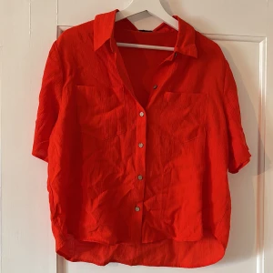 Röd skjorta från JDY - Säljer en röd skjorta från JDY i storlek L. Skjortan har korta ärmar, knappar framtill och två bröstfickor. Materialet är lätt och luftigt, perfekt för varmare dagar. Snygg att bära öppen eller stängd.
