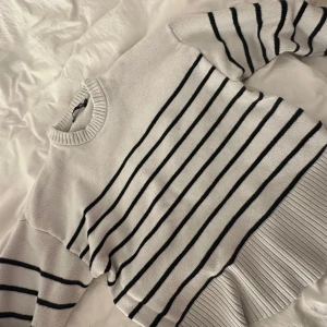 Vit och svart randig stickad tröja - Säljer en vit stickad tröja med svarta ränder. Tröjan har rund halsringning, långa ärmar och breda ribbade muddar vid ärmslut och nederkant. Perfekt för en stilren och avslappnad look.