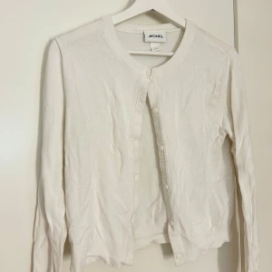 Vit kofta från Monki - Säljer en klassisk vit kofta från Monki med rund halsringning och knappar framtill. Tröjan har långa ärmar och är tillverkad i ett mjukt material som passar perfekt till lager-på-lager-stil.