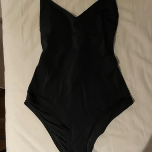 Svart baddräkt med v-ringning - Säljer en stilren svart baddräkt med v-ringad hals och smala axelband. Klassisk modell som passar perfekt för stranden eller poolen. Enkel och tidlös design.
