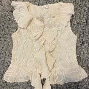 Krämvit volangtopp - Säljer en krämvit ärmlös topp från Gina Tricot med volangdetaljer längs halsringningen och nederkanten. Den är aldrig använd💗😊