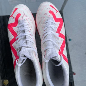 Fotbollsskor Puma  - Säljer ett par vita fotbollsskor från Puma med rosa detaljer och snörning. Skorna har en platt sula och är designade för inomhusspel men funkar lika bra utomhus 