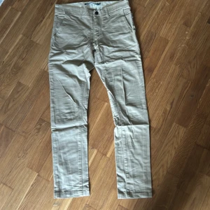 Beige chinos från WinWin köpt på Carlings - Snygga beige chinos från WinWin i bomull. Klassisk rak passform med knapp och dragkedja framtill samt fickor på sidorna. Perfekta för en stilren och avslappnad look.