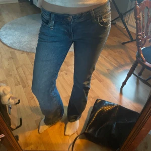 Blå jeans med broderad ficka - Säljer ett par klassiska blå jeans med normal passform och snygg broderad detalj på bakfickan. Jeansen har låg midja med utsvängda ben. Köpta secondhand men kom aldrig till användning. Finns en defekt (kolla bild).