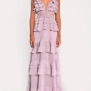 True decadence klänning  - Superfin ljuslila långklänning med djup v-ringning, volanger och spetsdetalj i midjan. Klänningen har smala axelband och flera lager volanger som ger en romantisk känsla. Perfekt för speciella tillfällen! Bara använt en gång!