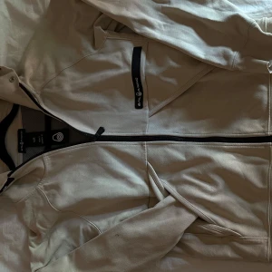 Sailracing Zip-hoodie - Denna zip-hoodie är en riktigt skön och snygg tröja, den är i beige färg och str S i man och M i kvinna. Den är unisex och är använd ett antal gånger men inga fel på tröjan, den är som ny helt enkelt