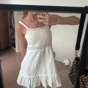 Vit somrig klänning - Söt vit klänning med broderade blommor och spetsdetaljer. Klänningen har smala axelband, volang nertill och är ärmlös. Från Zara i storlek XS