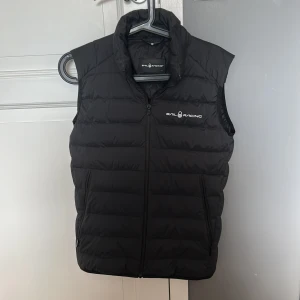 Svart dunväst från Sail Racing Junior - Säljer en svart dunväst från Sail Racing med dragkedja framtill och logga på brödet. Sitter som XS.