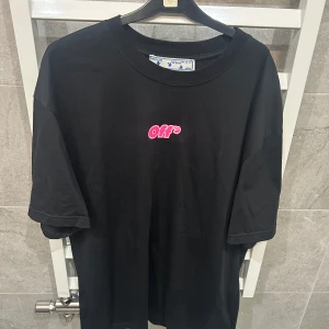 Svart t-shirt från Off-White med tryck - Svart t-shirt från Off-White med liten rosa 'off' text på bröstet och stort grafiskt tryck med figurer och texten 'WHITE' på ryggen. Klassisk rund hals och normal passform. Perfekt för dig som gillar streetwear och unika prints.