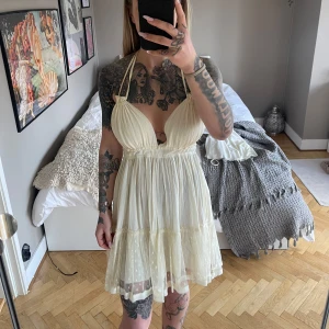 Klänning  - Supersöt cremefärgad klänning med volangdetaljer och knyt i ryggen. Klänningen är ärmlös, har djup v-ringning och är sydd i ett tunt, lätt material med diskret prickigt mönster på kjolen. Har små fläckar som inte syns alls vid användning (se bilder) passar allt från xs-L då man drar in den med snören. Jag har xs vanligtvis för referens på bilderna 