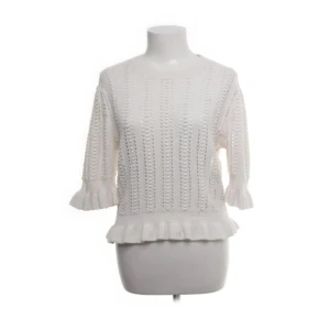 Vit stickad tröja med volang från Zara - Säljer en söt vit stickad tröja från Zara med volangdetaljer vid ärmslut och nederkant. Tröjan har trekvartsärm och ett luftigt, hålstickat mönster som ger en trendig look. Perfekt för lager-på-lager under kyliga dagar.