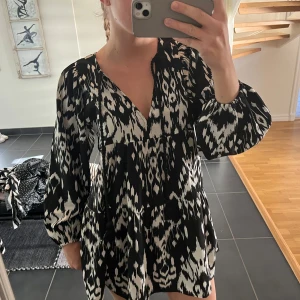 Svartvit mönstrad kortklänning - Kort klänning med svartvitt grafiskt mönster och v-ringning. Långa, luftiga ärmar och lös passform. 