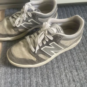 Grå New Balance sneakers BB480 - Säljer ett par grå New Balance BB480 sneakers i mocka och syntet med vita detaljer och snörning. Klassisk modell med rund tå och platt sula, perfekt för dig som gillar stilrena och sportiga skor. Ikoniskt N på sidan. 