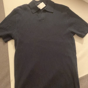 Mörkblå stickad pikétröja - Säljer en Mörkblå stickad pikétröja med klassisk krage och korta ärmar. Tröjan har en diskret ribbad struktur som ger en snygg och stilren look. Perfekt för dig som vill ha något enkelt men ändå trendigt.