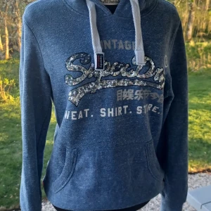 Blå hoodie från Superdry med paljettdetaljer - Säljer en blå hoodie från Superdry. Tröjan har huva och magficka 💙💦🪼Jag hade den när jag var yngre så jag skulle säga storlek xs/s. Välanvänd men fortfarande fint skick. Det är bara att skriva om man har frågor!😊💖