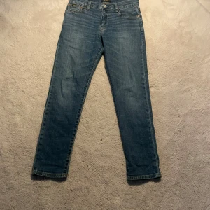 Blå jeans från Polo Ralph Lauren - Säljer ett par klassiska blå jeans från Polo Ralph Lauren. Jeansen har normal passform men lite mer åt slim hållet, raka ben och fem fickor. Perfekta för en stilren och avslappnad look. Tidlös design med snygga detaljer och gul söm.