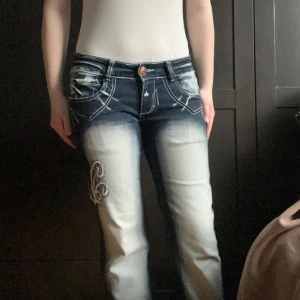 Crazy age liknande jeans - Mörkblå Blue queen jeans,med rhinestones och vitt mönster köpta i köpenhamn,några stenar saknas men inget man lägger märke till,den var redan uppsydda när jag köpte dem.Mått: midja (rakt över) 43 cm,höft 49 cm,innerben 68/69 cm