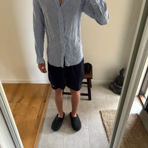 Blåvit randig skjorta från Ralph Lauren (pris diskuteras)  - Säljer en blåvit randig skjorta från Ralph Lauren med klassisk krage och knäppning framtill. Skjortan har långa ärmar och en gul broderad logga på bröstet. Perfekt för dig som gillar en stilren och fräsch look.