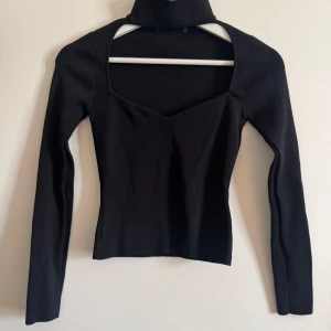 Svart ribbad öppen polo  - Trendig svart ribbad polotröja med lång ärm. Tröjan har en snygg u-ringning framtill och en tight passform som framhäver siluetten. Perfekt för dig som gillar en stilren men edgy look. 