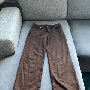 Bruna raka jeans från H&M Divided - Snygga bruna jeans från H&M Divided i rak modell. Byxorna är tillverkade i 100% bomull och har klassisk femficksdesign med knapp och dragkedja framtill. Perfekta för dig som gillar en avslappnad och stilren look.