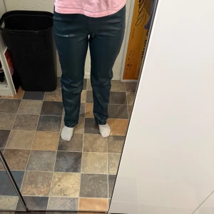 Mörkgröna skinnbyxor Gina Tricot - Snygga mörkgröna byxor i skinnimitation från Gina Tricot. Modellen är rak med normal passform och klassiska fickor fram och bak. Använda fåtal gånger och är i superfint skick!