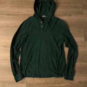 Mörkgrön hoodie från Polo Ralph Lauren - Priset kan diskuteras Mörkgrön hoodie från Polo Ralph Lauren med klassisk huva och knäppning vid halsen. Tröjan har långa ärmar, ribbade muddar och den ikoniska röda loggan broderad på bröstet. Tillverkad i mjuk bomull som känns skön mot huden.