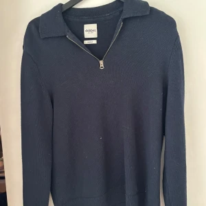 Mörkblå stickad tröja från Dobber - Mörkblå stickad tröja från Dobber i storlek medium. Tröjan har en klassisk krage och en half zip-dragkedja framtill. Långärmad och i mjukt material som passar perfekt till kyligare dagar. Enkel och stilren design som är lätt att matcha.