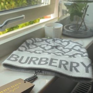 Vit och grå Burberry mössa - Snygg mössa från Burberry i vit och grå med ikoniskt mönster och stor logga framtill. Klassisk beanie-modell i mjukt stickat material, perfekt för att lyfta din stil🤩. Passar dig som vill ha en exklusiv och trendig accessoar😎✅