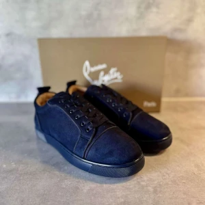 Mörkblå mocka sneakers från Louboutin - Snygga mörkblå sneakers i mocka från Christian Louboutin med klassisk röd sula och diskret logga på sidan. Skorna har rund tå, svarta snören och en stilren design som sticker ut med den ikoniska röda undersidan.