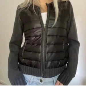 jacka - Snygg pufferjacka i svart och grått med quiltad front och stickade ärmar. Jackan har dragkedja framtill och ribbade muddar. Perfekt för dig som vill ha en sportig men ändå stilren look.