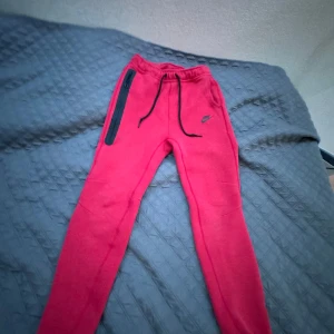 Röda Nike mjukisbyxor med dragkedja - Snygga röda mjukisbyxor från Nike med svart logga på benet. Byxorna har svarta snören i midjan och en lång svart dragkedja på ena benet. Perfekta för chill eller träning, tillverkade i mjukt material för maxad komfort. Äkta!!!