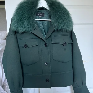 Grön pälsjacka från Meotine XS/S - Säljer en mörkgrön jacka från Meotine med stor fluffig rävpäls-krage. Jackan har två stora bröstfickor med knappar och en boxig, croppad passform. Materialet är polyesterblandning och fodret är mjukt. Perfekt statement-plagg för höst och vinter.