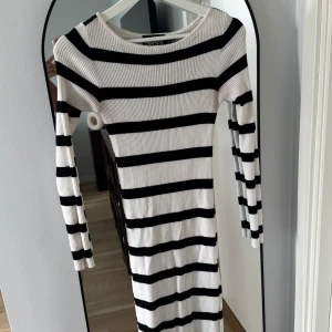 Randig ribbad klänning från Pieces - Säljer en långärmad, ribbad klänning från Pieces med svartvita horisontella ränder. Klänningen är figurnära och har en liten slits nertill. Perfekt för dig som gillar en enkel men snygg look.
