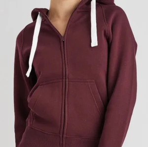 Vinröd hoodie russemerch - Vinröd hoodie med vit snörning och dragkedja framtill. Tröjan har huva, känguruficka och är tillverkad i mjuk bomullsmix. Som i nyskick använd max 3 gånger i kort perioder och säljer då jag har en till. Den har små fläckar på ena sidan huvan men inget man tänker på när man använder den. Osäker om det går bort i tvätt så jag inte provat. Nypris 700kr