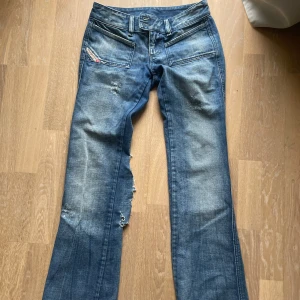 Blå bootcut jeans från Diesel - Midjemått ca37. Jag är en 163 för referens. Snygga blå jeans från Diesel med slitningar och stor reva längs benet. Modellen har låg midja, raka ben med bootcut och coola detaljer på fickorna. Det är ett hål nere p byxan som ni ser på bilden. 