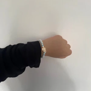 Blåvitt pärlarmband med snäcka - Superfint armband med blå och vita pärlor och en liten snäcka som detalj. Armbandet har ett smidigt spänne i silverfärg och passar perfekt för dig som gillar strandvibbar och somriga accessoarer. Vi har tre av denna sort.
