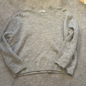 Grå stickad tröja med pärlor H&M - Superfin grå stickad tröja från H&M med pärldetaljer på axlarna. Tröjan har rund halsringning, långa ärmar och ribbade muddar. Perfekt för dig som gillar en enkel men ändå lite extra look.