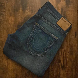 True Religion Jeans - Säljer ett par äkta True Religion jeans i storlek W32. Klassisk modell med snygga detaljer och ikoniska sömmar. Bra skick utan större slitningar eller fläckar. Perfekta för dig som vill ha en stilren men edgy look. Nypris ca 2000–2500 kr.