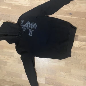 Svart hoodie från Mercier XS - Svart hoodie från Mercier i storlek XS med coola patch-detaljer på bröstet och snörning i huvan. Klassisk känguruficka framtill och långärmad modell. Perfekt för dig som gillar streetwear och vill ha en stilren look. Dm vid intresse😃