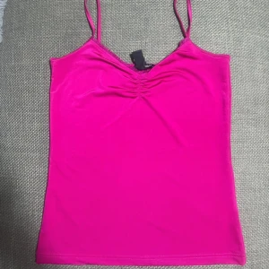 Rosa linnetopp från H&M - Säljer en snygg rosa linnetopp från H&M med smala axelband och rynkdetalj vid bysten. Toppen är figurnära och har en enkel, stilren design som passar perfekt till sommaren. Materialet känns mjukt och stretchigt.