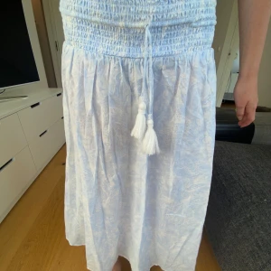 Ljusblå långkjol från Gina Tricot - Supersöt ljusblå långkjol från Gina Tricot med smock i midjan och knytband med glitter tofsar. Gjord i ett lätt och luftigt bomullstyg, perfekt för varma dagar.