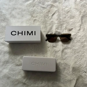 Bruna solglasögon från CHIMI - Snygga solglasögon från CHIMI med fyrkantig form och bruna glas. Bågarna är mörkbruna och tillverkade i plast. Kommer med originalbox och fodral. Perfekta för dig som vill ha en stilren och modern look.