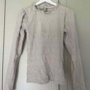 Beige långärmad blus från ONLY - Supersöt beige blus från ONLY i storlek XS. Blusen har lång ärm, rynkad struktur och volangdetalj vid halsen. Perfekt för dig som gillar en romantisk och trendig stil. Passar lika bra till jeans som till kjol.