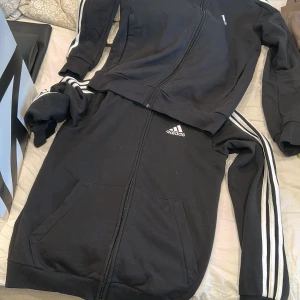 Svart Adidas zip-hoodie med ränder - Svart Adidas hoodie med dragkedja och klassiska vita ränder längs ärmarna.  Har två likadana, i storlek S. Säljs 70kr styck