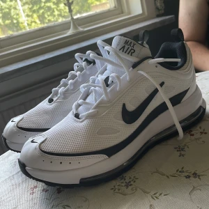 Nike Air Max vita sneakers strl 44 - Snygga Nike Air Max sneakers i vitt med svarta detaljer och klassisk swoosh. Ovandel i mesh och syntet, svart innersula och tydlig Air Max-dämpning i sulan. Perfekta för dig som gillar sportig och clean stil. Skorna har snörning och rund tå. Aldrig använda. Nypris 1.600 kr