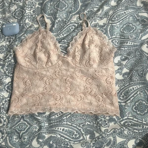 Beige spetsig linnetopp med blommönster - Supersöt beige linnetopp med blommig spets och tunna axelband. Toppen har v-ringning och fina spetsdetaljer längs kanterna.