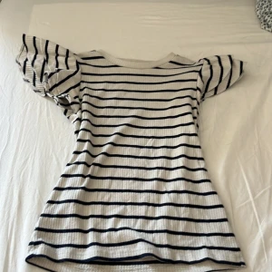 Randig topp med puffärm Holly & Whyte - Supersöt topp från Holly & Whyte med marinblå och vita ränder. Den har korta puffärmar och är ribbad i materialet, vilket ger en snygg struktur. Perfekt för dig som gillar en klassisk men trendig look.