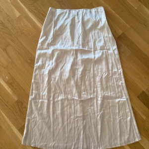 Vit långkjol i satin-look - Enkel och stilren vit långkjol med lätt glansig satin-feeling. Kjolen har rak passform och faller snyggt längs benen. Perfekt att styla med en crop top eller oversized tröja för en clean look. Är helt ny men har ingen prislapp